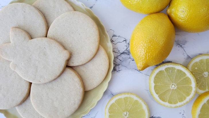 Lemon shortbread sugar cookies arranged on a yellow plate next to fresh lemons.