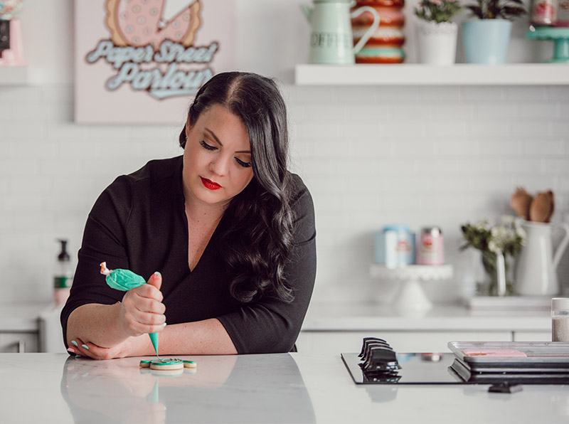 Photo of Tyler April Townley of Paper Street Parlour decorating a cookie in a clean modern kitchen