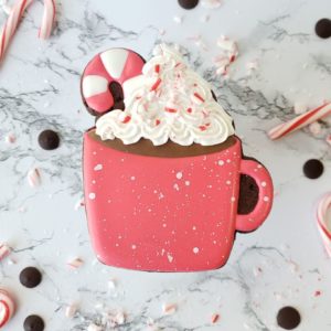 A chocolate candy cane shortbread sugar cookie decorated to look like a mug of hot coco with a candy cane and whipped cream.