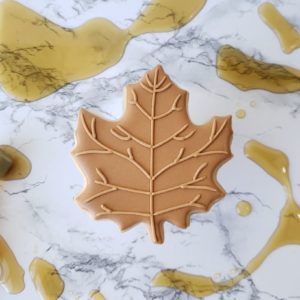 A maple shortbread sugar cookie decorated to look like a maple leaf.