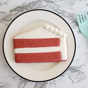 A red velvet shortbread sugar cookie decorated to look like a slice of red velvet cake