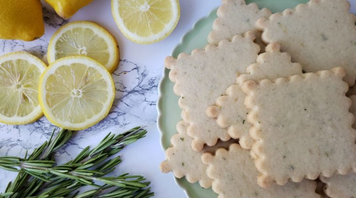 Lemon rosemary shortbread sugar cookies on a mint green plate, next to sliced fresh lemon, and fresh rosemary. 