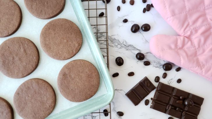 Mocha shortbread sugar cookies on a mint green cookie sheet next to chocolate bars and coffee beans. 