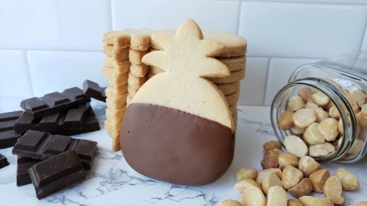 a single chocolate dipped, pineapple shaped, macadamia nut cookie, leaning against a stack of more cookies