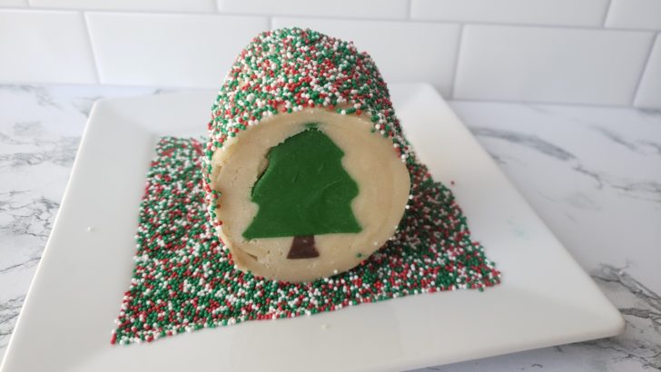 A log of cookie dough with a Christmas tree center design, rolled in Christmas sprinkles.