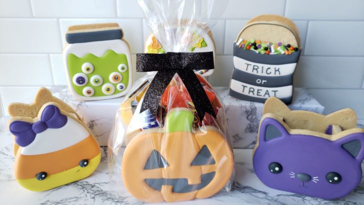 Halloween treat boxes made from decorated cookies and filled with Halloween candy. One treat box is packaged in a bag tied with a black ribbon.