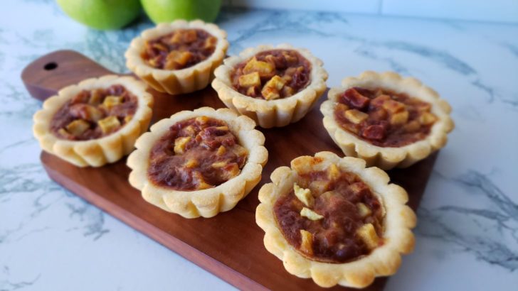6 apple pie tartlets on a small wooden board. 