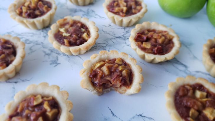 Baked apple pie tartlets sitting on a marble surface. 
