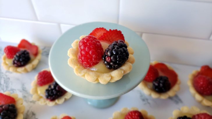 A fruit tarts with lemon curd, blackberries, raspberries, and strawberries, sitting on mini light blue dessert stand. 
