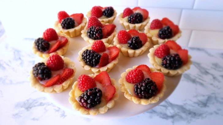 Fruit tarts with lemon curd, blackberries, raspberries, and strawberries, sitting on cake stand. 