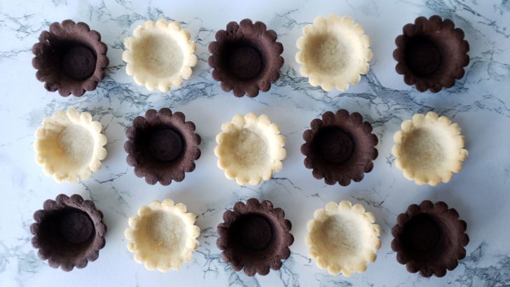 Vanilla and chocolate empty tartlet shells sitting on a marble counter.
