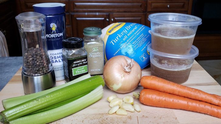 Ingredients for a roast turkey. Frozen turkey, stock, an onion, carrots, garlic cloves, celery stalks, salt, pepper, sage and thyme. 