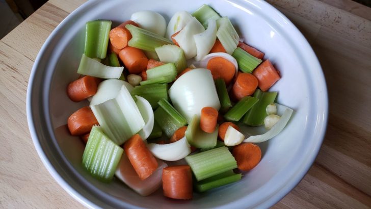 Chopped carrots, celery, onion and garlic cloves in a large white pie pan. 