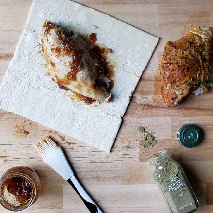 a turkey breast covered in fig jam and sage sitting on a sheet of puff pastry. 
