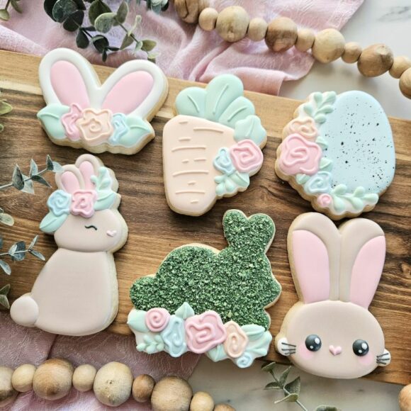 Decorated Easter cookies sitting on a wooden surface. 3 different bunnies, a carrot, an egg, and bunny ear cookies.